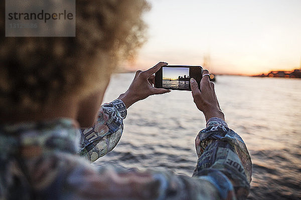 Ausschnitt einer Frau  die mit einem Smartphone das Meer fotografiert