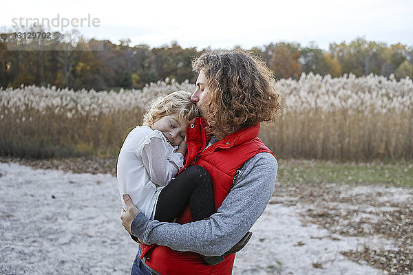 Mutter küsst Tochter  während sie im Winter auf dem Feld gegen den Himmel steht