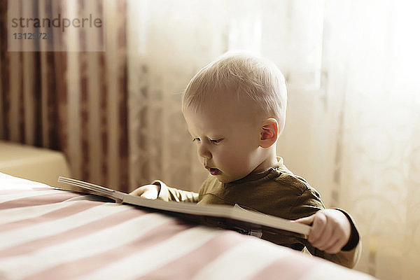 Nahaufnahme eines Jungen  der ein Buch liest  während er zu Hause am Bett steht