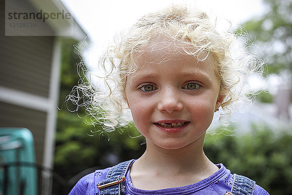 Nahaufnahme-Porträt eines süßen Mädchens mit unordentlichem blonden Haar  das im Hof gegen den Himmel steht