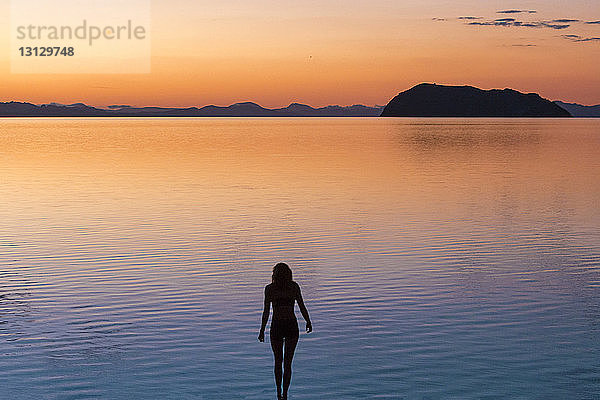 Silhouette einer Frau  die bei Sonnenuntergang am Meer steht