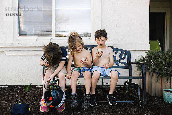 Geschwister essen Äpfel  während sie auf einer Bank im Hinterhof sitzen