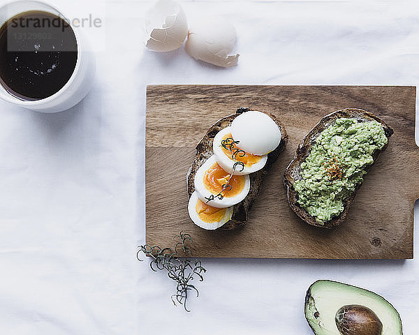 Draufsicht auf gekochte Eier und Avocadopastete auf Broten mit Kaffee