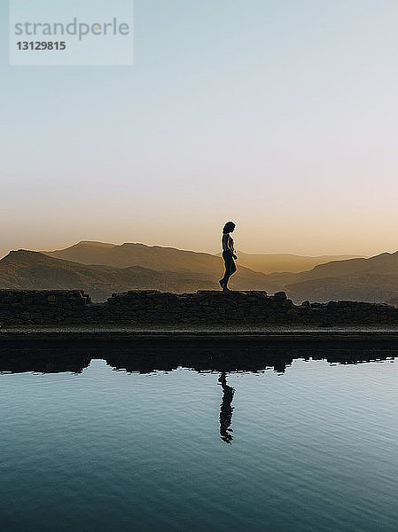 Frau reflektiert sich bei Sonnenuntergang am See gegen den klaren Himmel