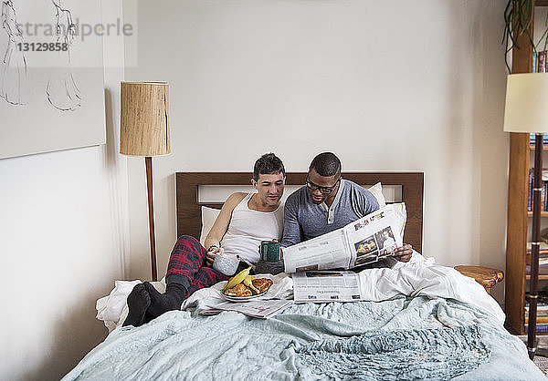 Multi-ethnische homosexuelle Männer  die im Schlafzimmer Zeitung lesen