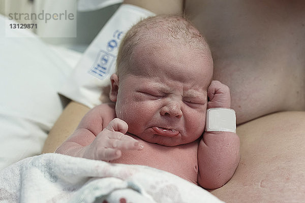 Nahaufnahme eines neugeborenen weinenden Sohnes durch hemdlose Mutter im Krankenhaus