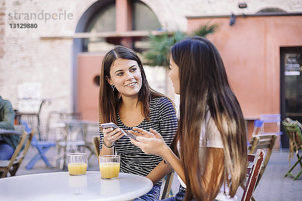 Freunde unterhalten sich während der Benutzung von Mobiltelefonen im Straßencafé