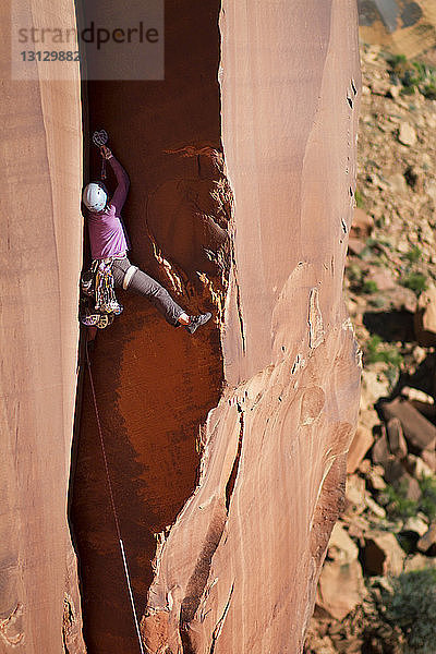 Rückansicht einer Bergsteigerin beim Klettern auf felsigen Berg