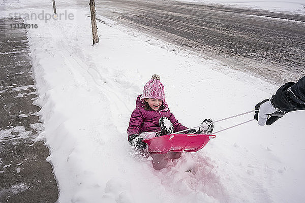 Abgehackte Hand eines Vaters  der seine Tochter im Schlitten sitzend auf schneebedeckter Straße zieht