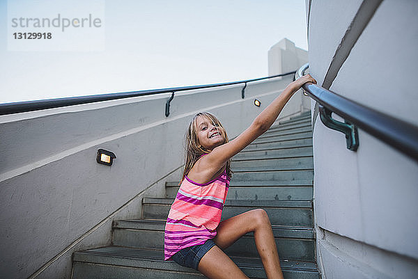 Porträt eines glücklichen Mädchens  das auf Stufen gegen den klaren Himmel spielt