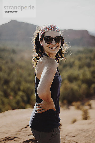 Lächelnde junge Frau steht auf einem Felsen gegen Berge