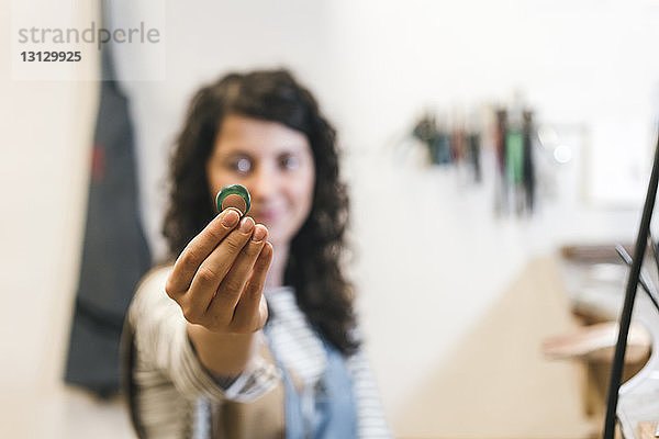 Porträt einer Kunsthandwerkerin  die einen Ring zeigt  während sie in einer Werkstatt an der Wand steht