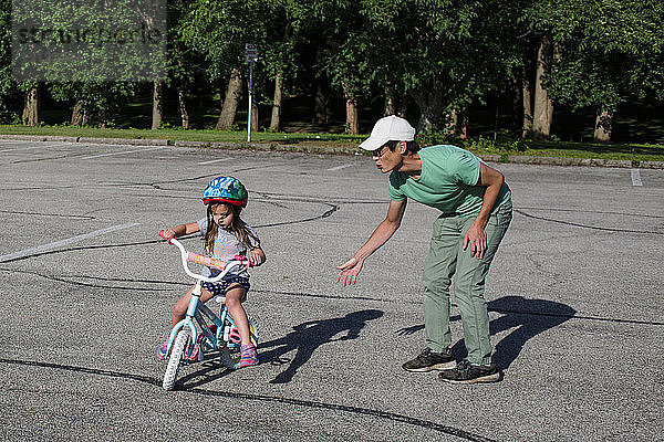 Vater bringt Tochter bei  bei Sonnenschein auf dem Spielplatz Fahrrad zu fahren