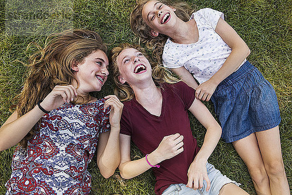 Draufsicht auf glückliche Geschwister  die auf einem Grasfeld im Park liegen