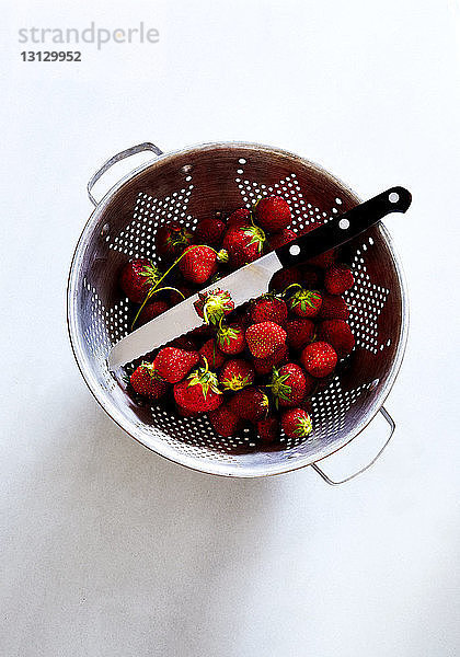 Draufsicht auf Erdbeeren und Küchenmesser in Sieb auf weißem Hintergrund