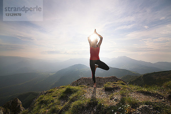 Frau praktiziert Yoga  während sie auf Berg gegen Himmel steht