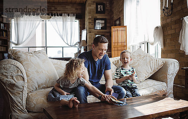 Glücklicher Vater spielt mit Kindern  während er auf dem Sofa im Wohnzimmer sitzt