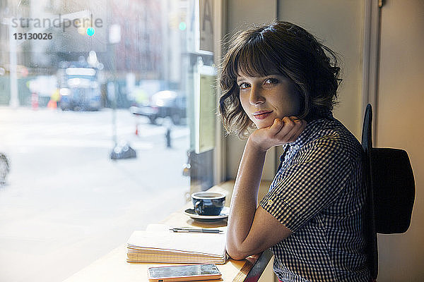 Porträt einer selbstbewussten Frau mit Hand am Kinn sitzend im Cafe