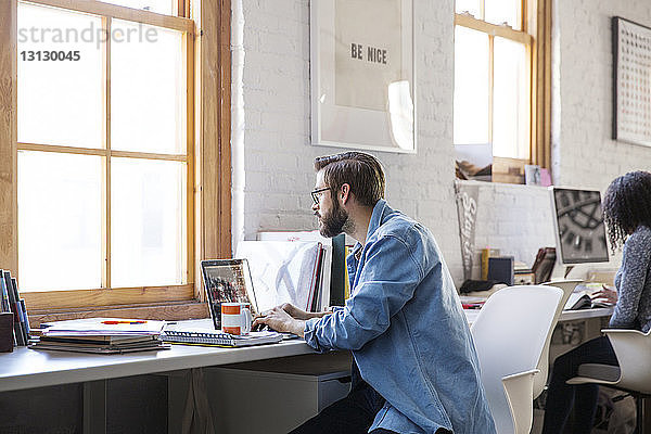 Geschäftsmann benutzt Laptop  während er am Schreibtisch im Kreativbüro sitzt