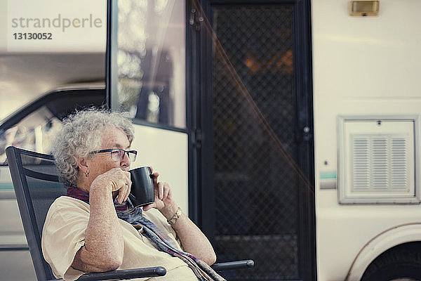 Seitenansicht einer älteren Frau  die Kaffee trinkt  während sie gegen einen Wohnwagen sitzt