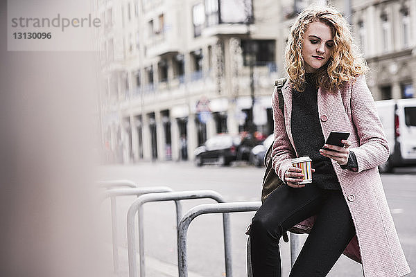 Geschäftsfrau benutzt Smartphone  während sie in der Stadt am Geländer sitzt