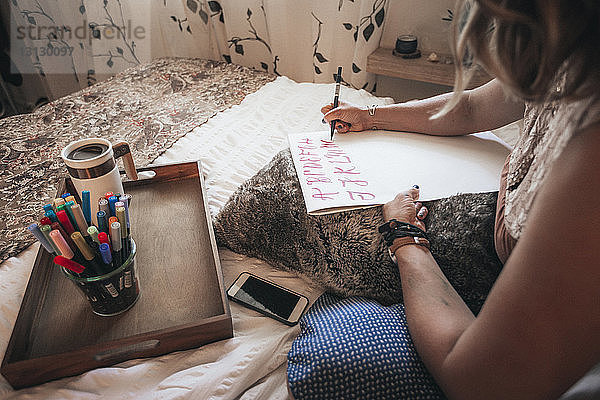 Beschnittenes Bild eines Künstlers  der zu Hause auf dem Bett sitzend Kalligrafie macht