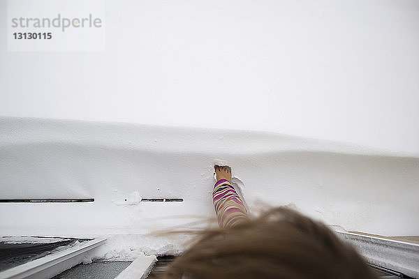 Draufsicht eines Mädchens  das mit dem Fuß den Schnee berührt