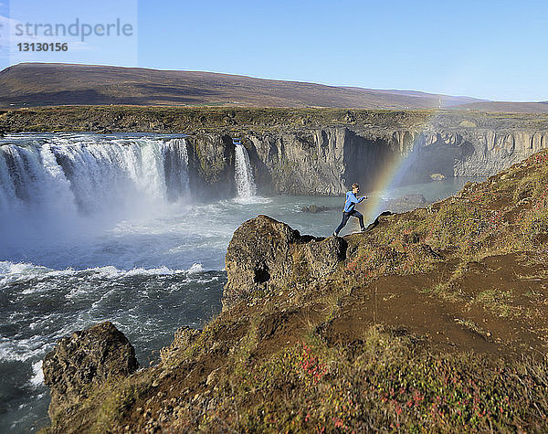 Seitenansicht eines Wanderers  der auf einem Berg gegen Wasserfall und Regenbogen läuft