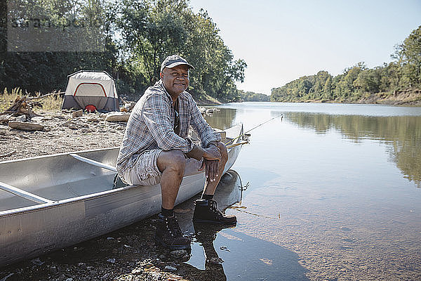 Porträt eines lächelnden Mannes  der auf einem Boot am Seeufer sitzt