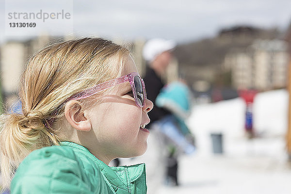 Seitenansicht eines Mädchens mit Sonnenbrille  das im Winter gegen den Himmel steht