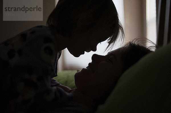 Scherenschnitt Mutter und Tochter schauen einander an  während sie sich zu Hause im Bett entspannen