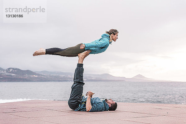 Freunde in voller Länge beim Üben von Akroyoga auf der Strandpromenade