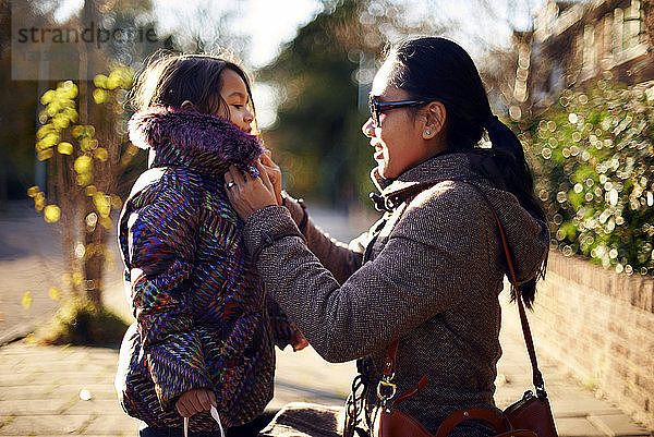 Mutter hilft Tochter beim Tragen des Wintermantels am Fussweg