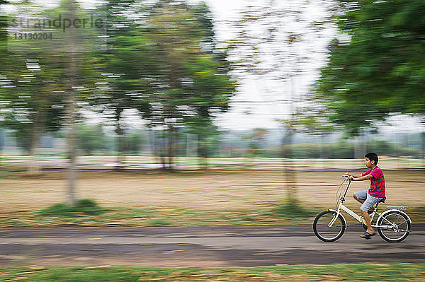 Verschwommene Bewegung eines Jungen  der Fahrrad auf einer Straße im Park fährt