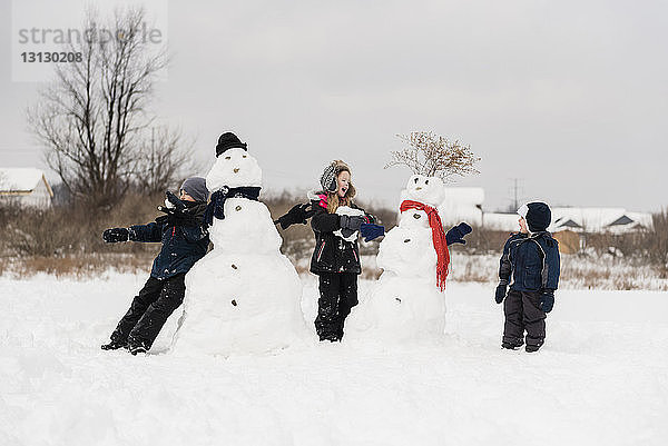 Geschwister spielen im Winter mit dem Schneemann