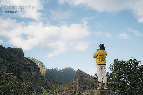 Rückansicht einer Frau  die auf einem Felsen stehend gegen den Himmel fotografiert