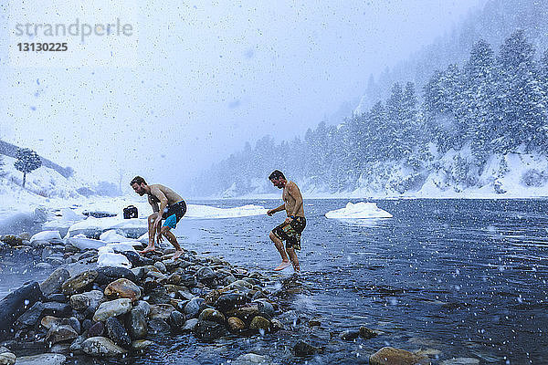 Männer gehen bei Schneefall auf Steinen im Fluss