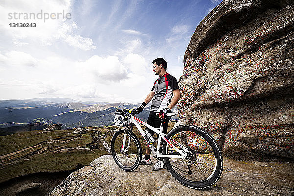 Männlicher Athlet mit Fahrrad auf Berg gegen Himmel stehend
