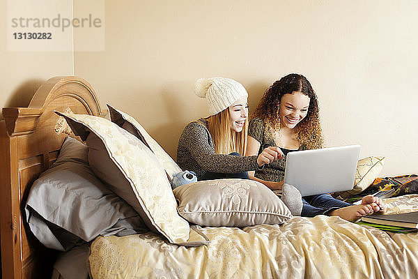 Glückliche Freunde  die zu Hause im Bett sitzen und einen Laptop benutzen