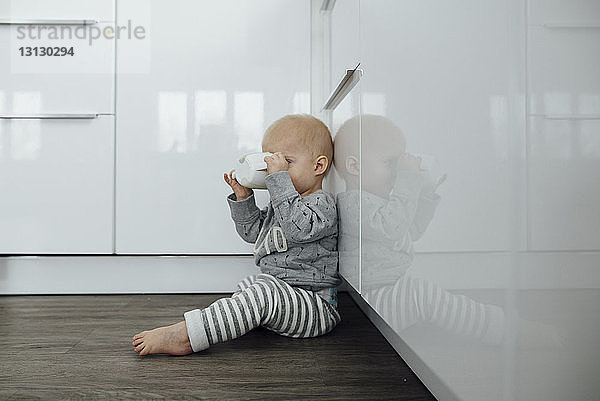 Seitenansicht eines kleinen Jungen  der trinkt  während er zu Hause auf dem Boden sitzt