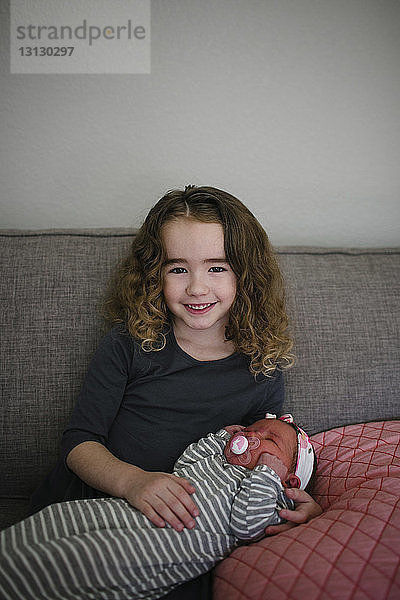 Porträt eines lächelnden Mädchens mit Schwester zu Hause auf dem Sofa sitzend