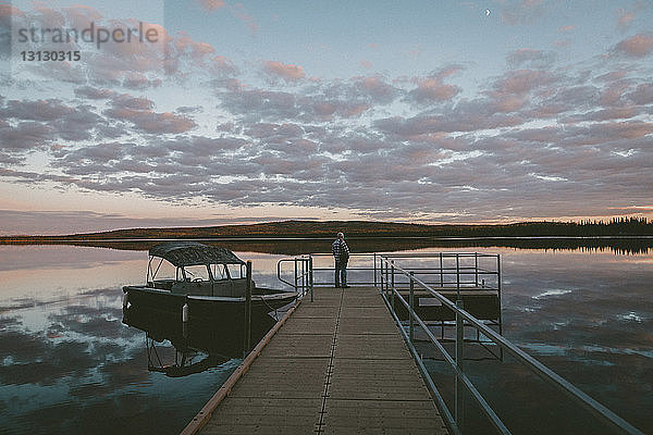 Mann steht bei Sonnenuntergang am Pier über dem Fluss vor bewölktem Himmel