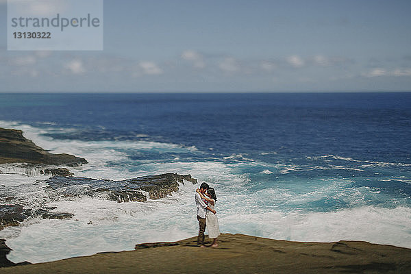 Seitenansicht eines Paares  das sich anschaut  während es am Strand gegen den Himmel steht