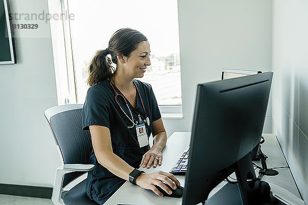 Lächelnde Ärztin benutzt Desktop-Computer im Krankenhaus