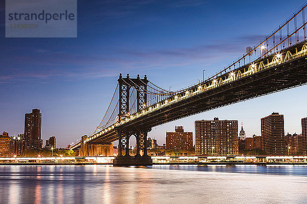 Tiefwinkelansicht der beleuchteten Manhattan Bridge über den East River gegen blauen Himmel in der Dämmerung