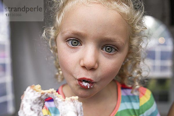 Porträt eines süßen Mädchens  das beim Donut-Essen ein Gesicht macht