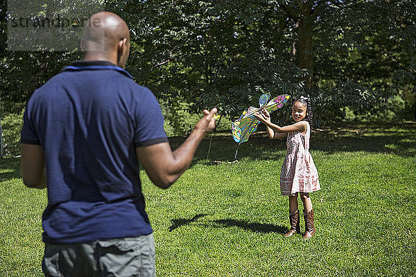 Glückliche Tochter und Vater spielen mit Drachen auf Grasfeld
