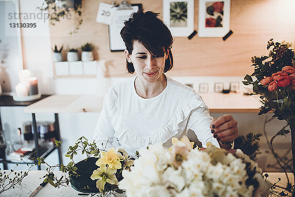 Lächelnder Florist arrangiert Blumen auf Blumenschaum bei Tisch im Laden