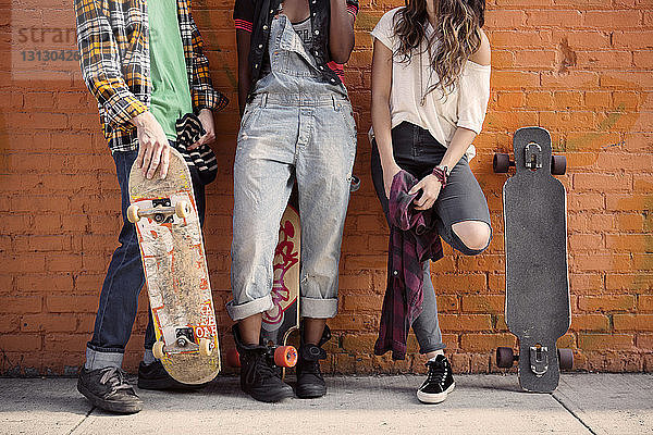 Niedrige Sektion von Freunden  die mit Skateboards an einer Ziegelmauer stehen