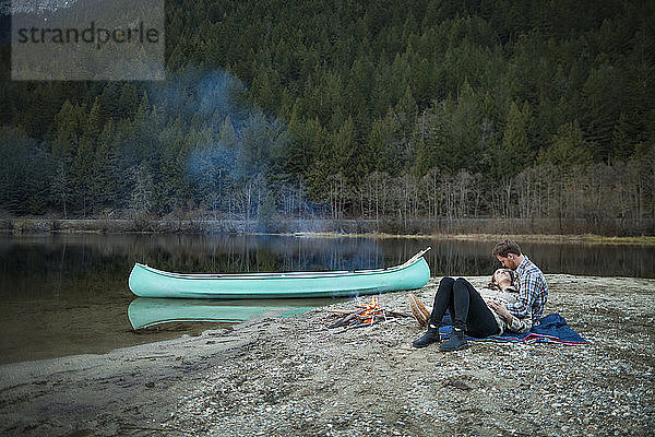 Ehepaar rastet in voller Länge am Lagerfeuer am Seeufer im Silver Lake Provincial Park